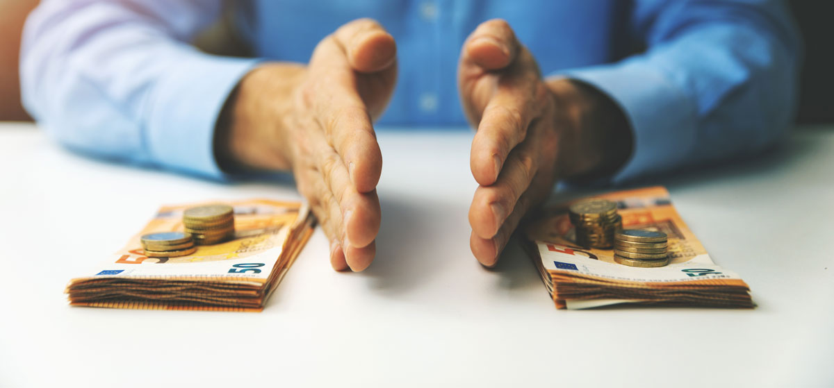 Mann an Tisch, der mit seinen Händen zwei Stapel mit Geldscheinen und -münzen trennt; symbolisch für die „CO2-Steuer“ für Vermieter.