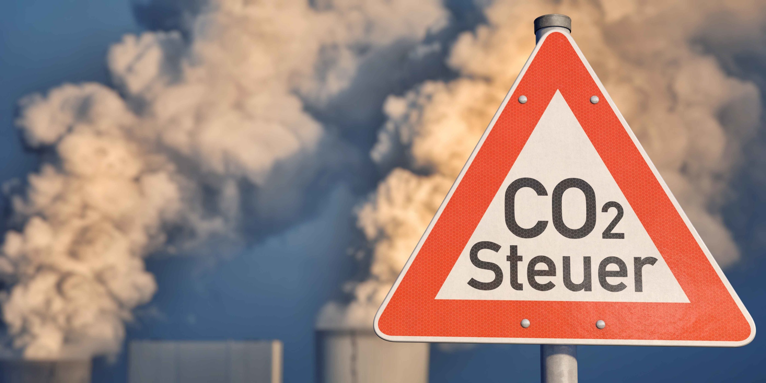Verkehrsschild „Vorsicht vor CO2-Steuer" vor Kühltürmen eines Kraftwerks.