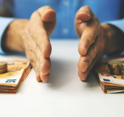 Mann an Tisch, der mit seinen Händen zwei Stapel mit Geldscheinen und -münzen trennt; symbolisch für die „CO2-Steuer“ für Vermieter.