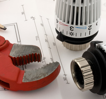 Zollstock, Bleistift, Rohrzange und zwei Thermostate auf dem Grundriss eines Hauses, symbolisch für die Heizungs-Austauschpflicht.