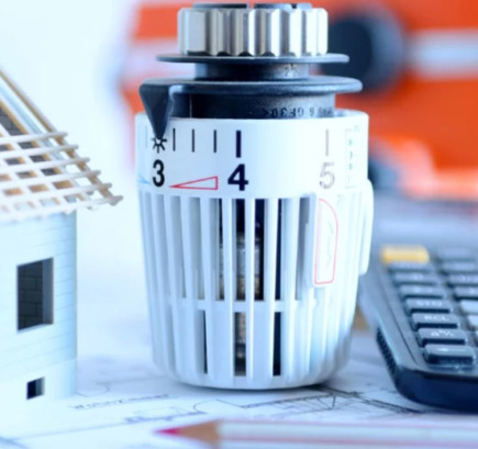 Modell eines Hauses, Heizkörperthermostat und Taschenrechner, symbolisch für die Heizungsmodernisierung.